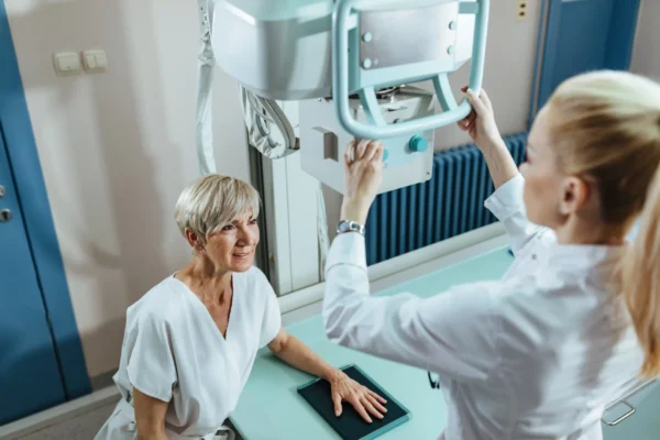 Medical technician assisting a mature female patient during an X-ray examination at the clinic.