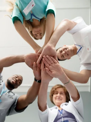 A diverse team of healthcare professionals standing in a circle, stacking their hands together in a show of unity and support.