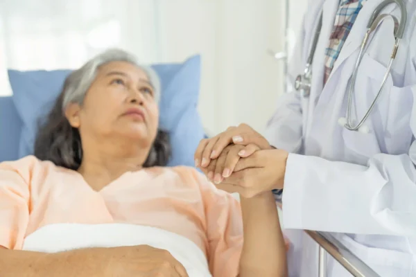A doctor holds hands with a senior woman in a hospital bed, offering emotional support.