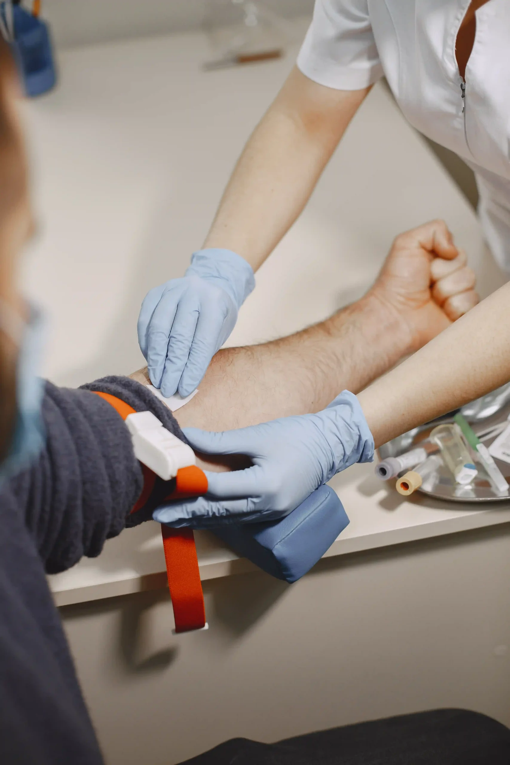 Nurse wearing gloves preparing a male patient’s arm for a blood draw in a clinic.