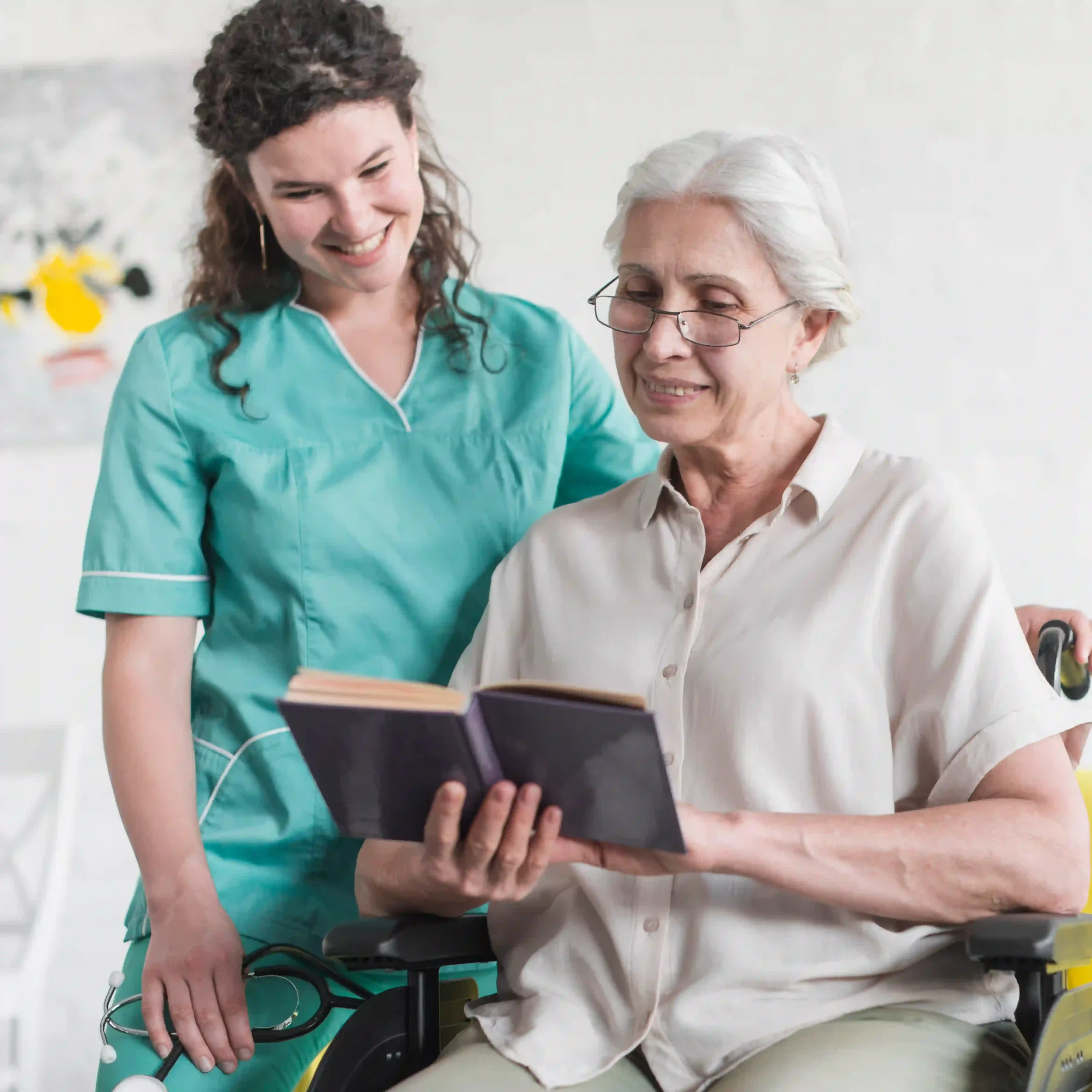Smiling nurse assisting a senior woman in a wheelchair with reading a book in a comforting care environment.