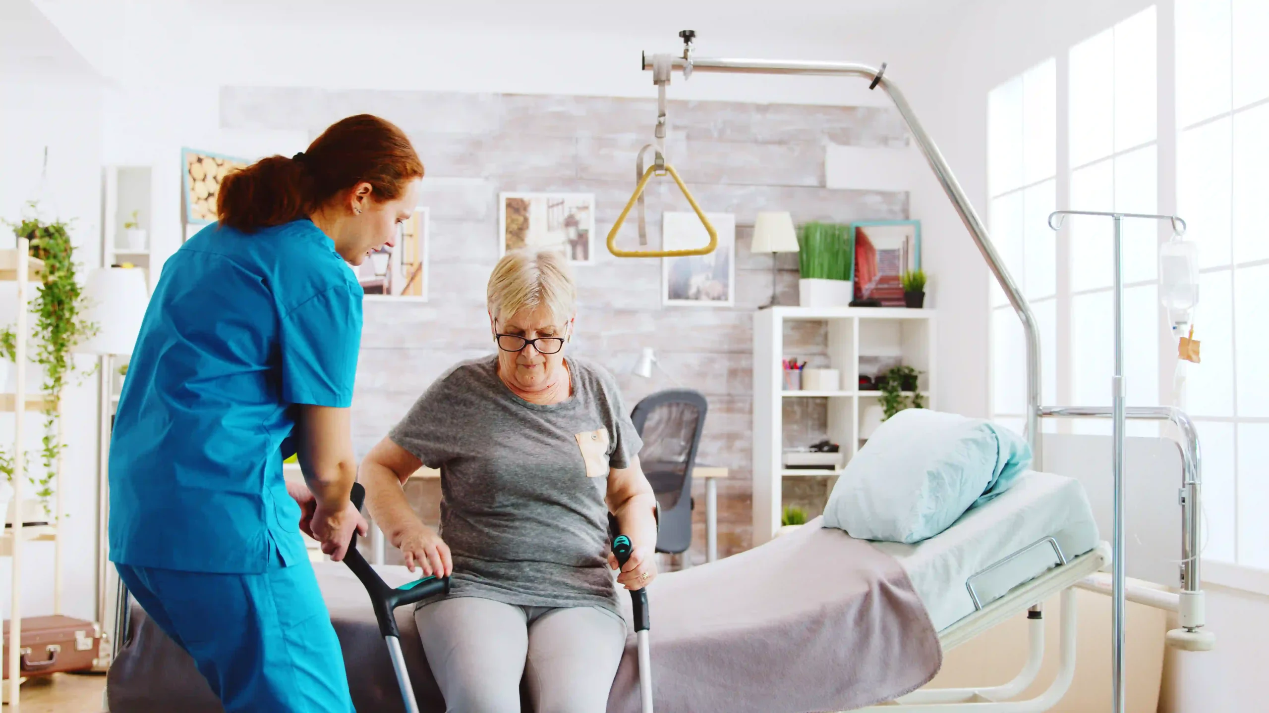 Elderly woman using crutches with nurse support during physical rehabilitation in a nursing home.