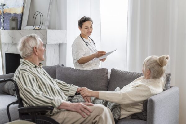Doctor consulting with an older couple at home, both seated on a couch and holding hands.