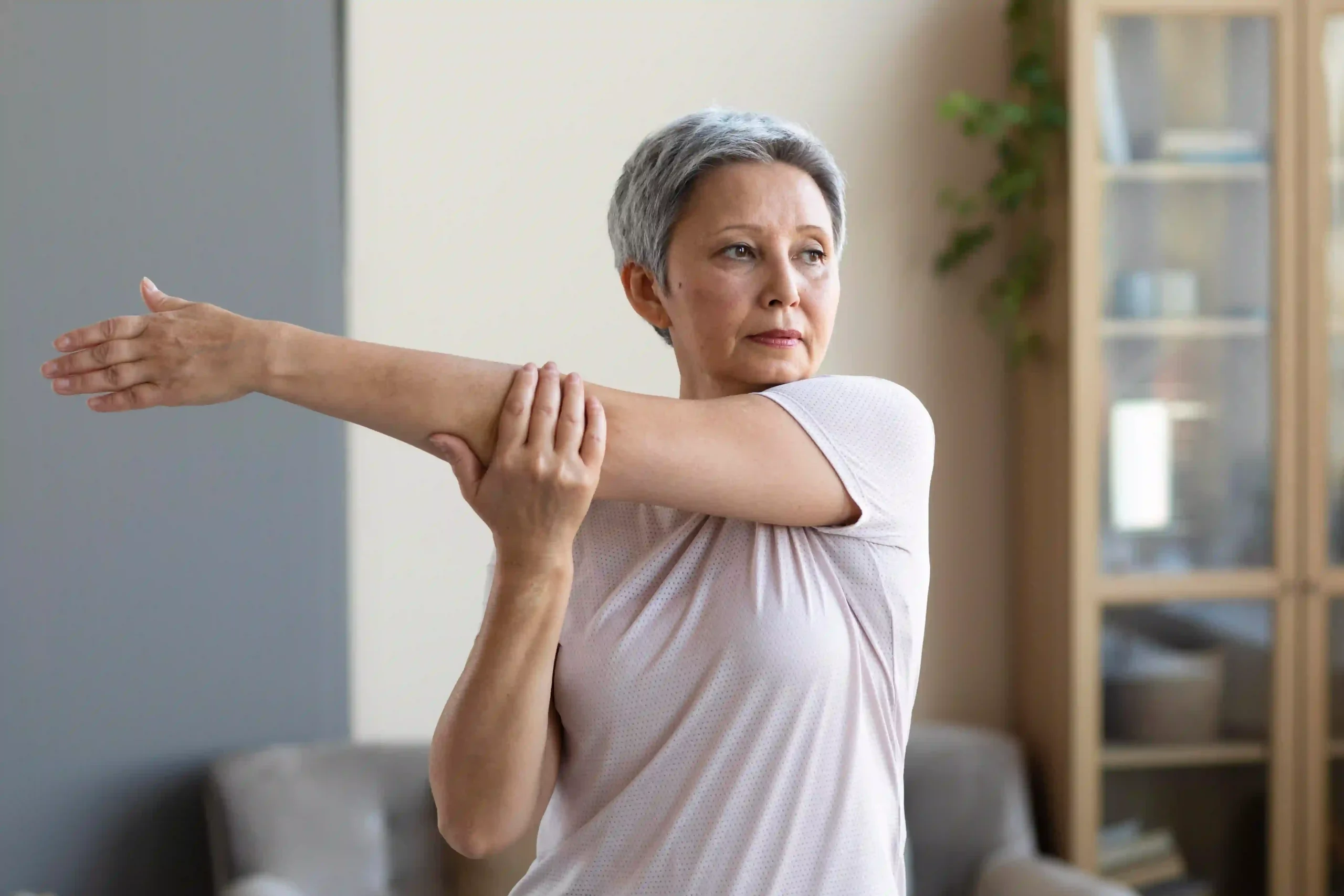 Older woman doing arm stretch at home as part of bone-strengthening exercise routine