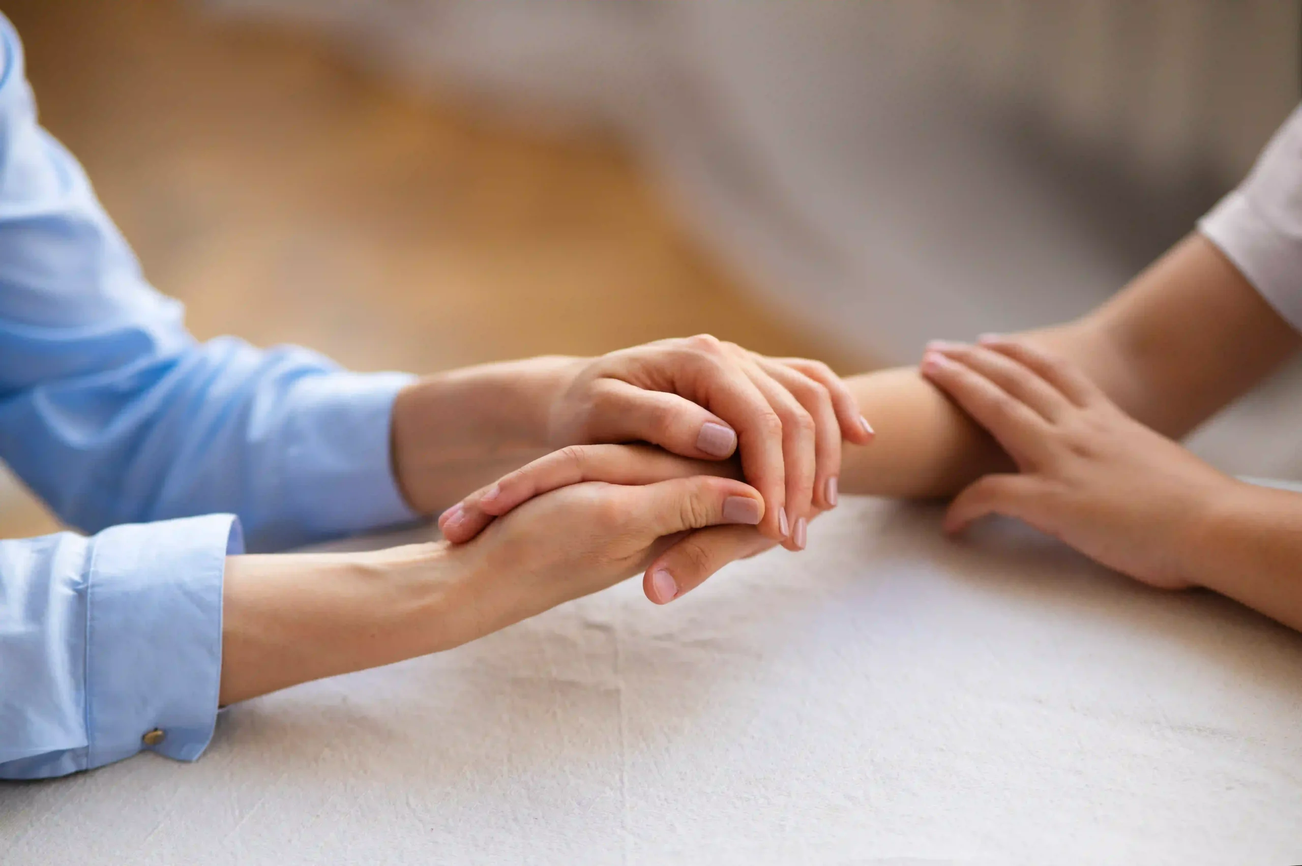 Two people holding hands with compassion at home, offering emotional support.