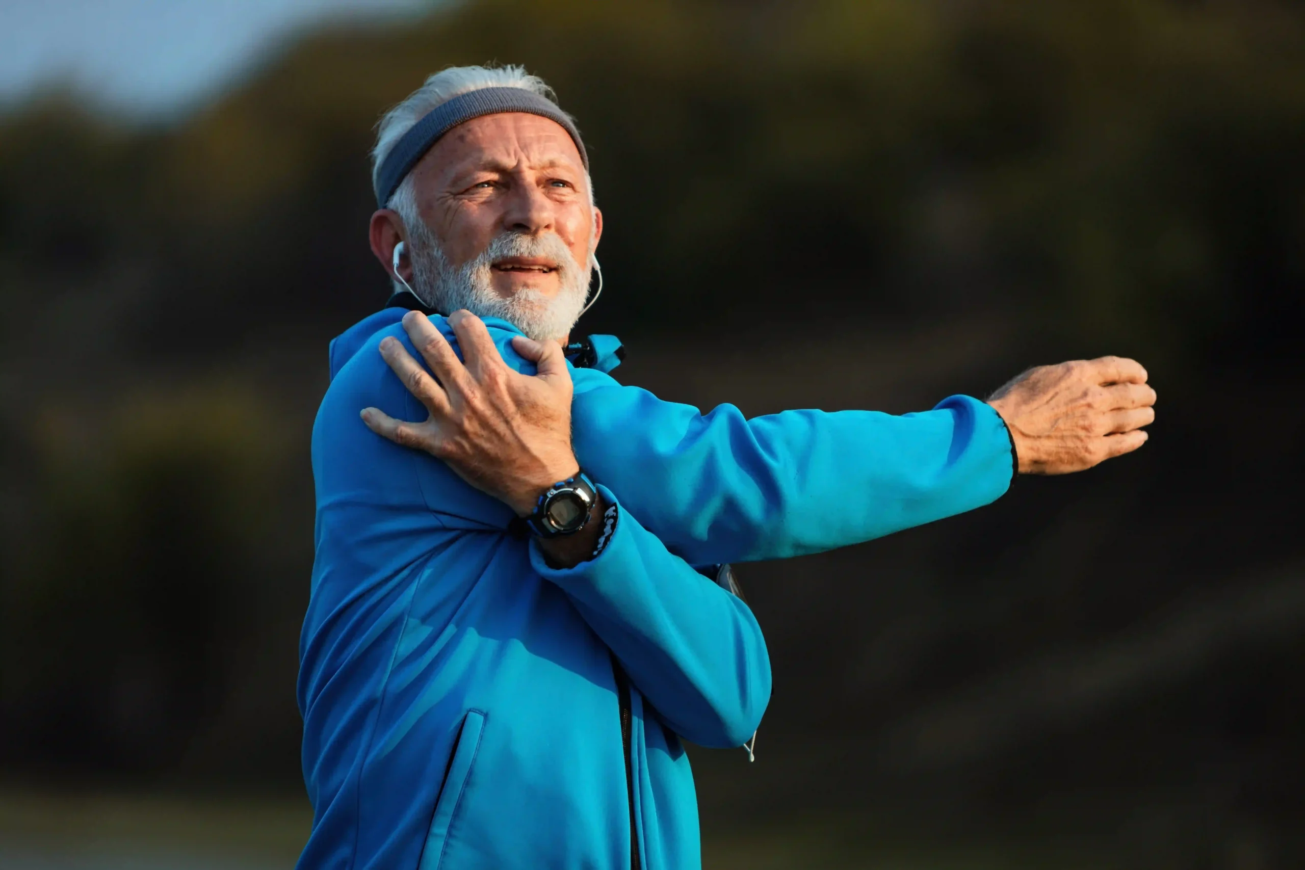 Older adult man stretching his shoulder outdoors, symbolizing joint mobility and orthopedic wellness in active aging