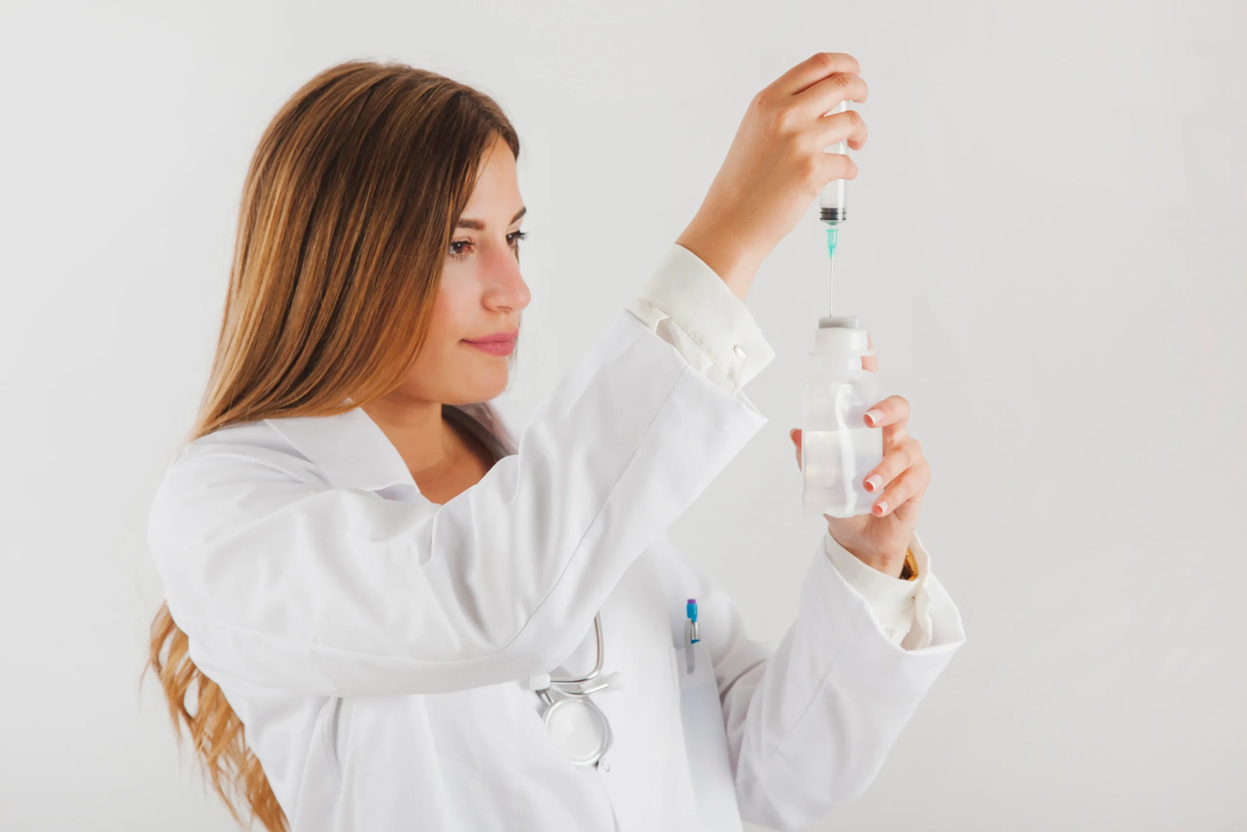 Female doctor in white coat drawing medication into a syringe from a vial.