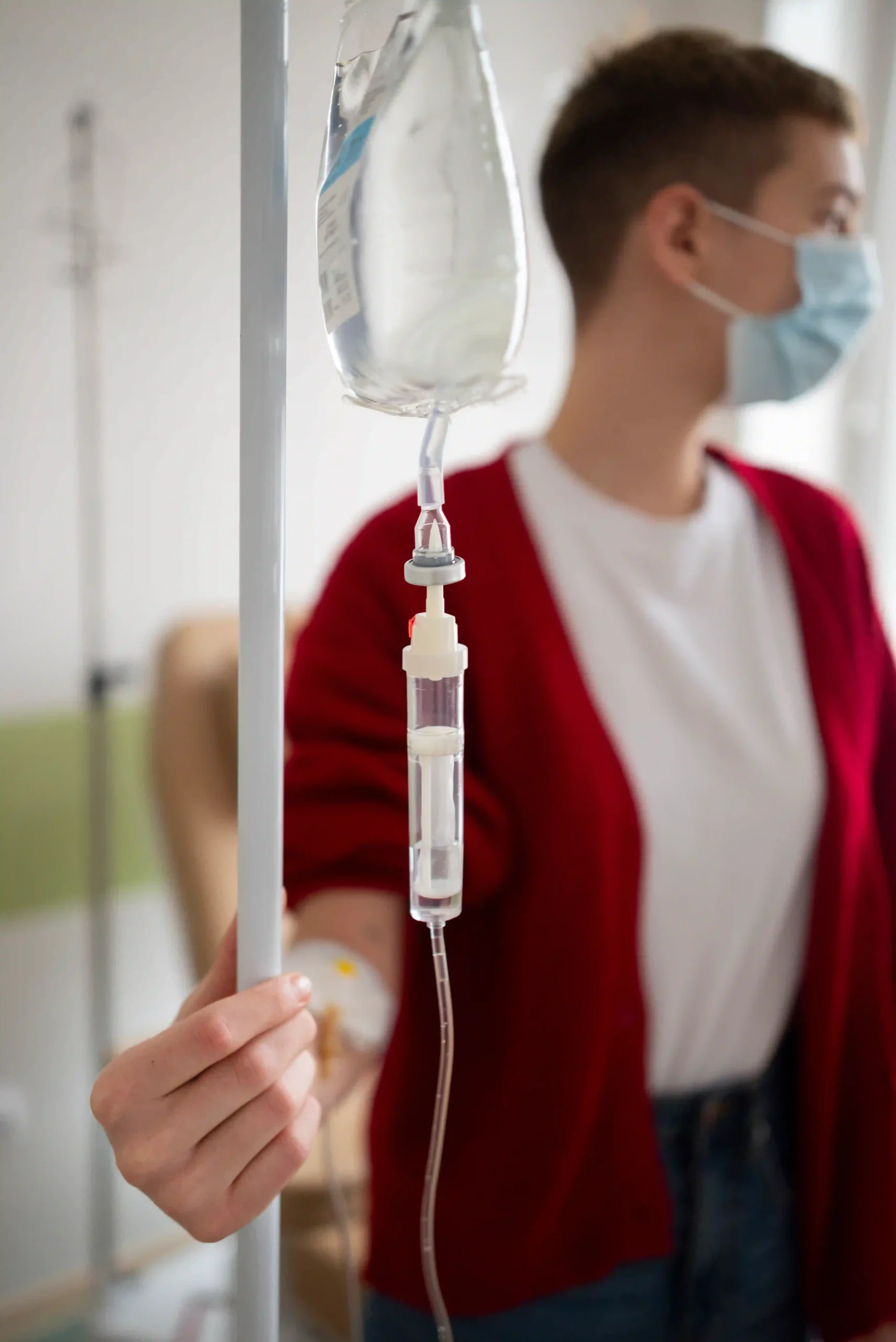 Close-up of IV drip with patient wearing mask during chemotherapy treatment.