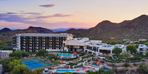 Aerial view of ADERO Scottsdale Resort, Autograph Collection at sunset with pools, tennis courts, and surrounding desert mountains.