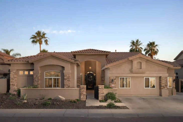 Exterior view of A & I Adult Care Home in Scottsdale, AZ at sunset, showing a modern stucco building with tile roof and palm trees in the background.