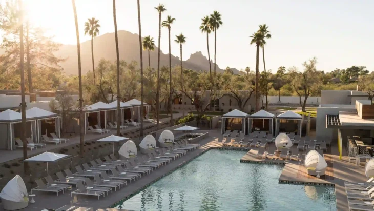 Outdoor pool area at Andaz Scottsdale Resort & Bungalows with cabanas, palm trees, and Camelback Mountain view at sunset.