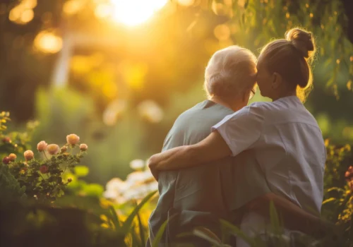 Elderly resident and caregiver embracing in a peaceful garden at sunset, symbolizing compassion and support at Aberdeen Home.