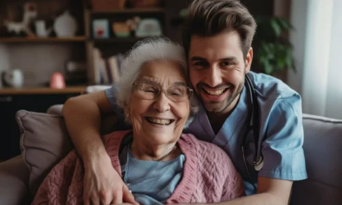 Smiling elderly woman and young male nurse sitting together in an assisted living home