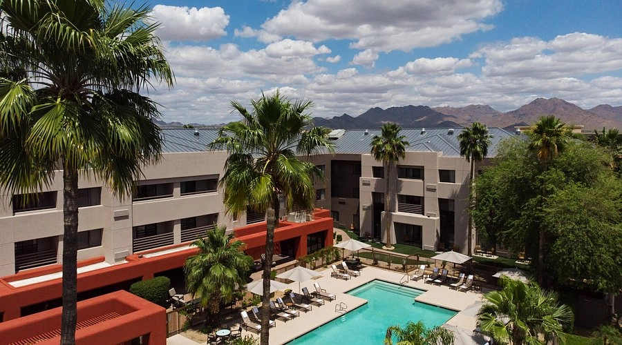 Outdoor view of Courtyard by Marriott Scottsdale North with swimming pool, palm trees, and mountain backdrop under blue sky.