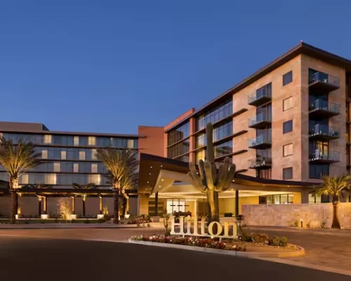 Evening exterior of Hilton North Scottsdale at Cavasson hotel, showing illuminated façade, desert landscaping, and signature Hilton entrance
