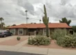Single-story assisted living home in Scottsdale with a stone exterior, red tile roof, large cactus plants in the front yard, and a parked SUV in the driveway under cloudy skies.