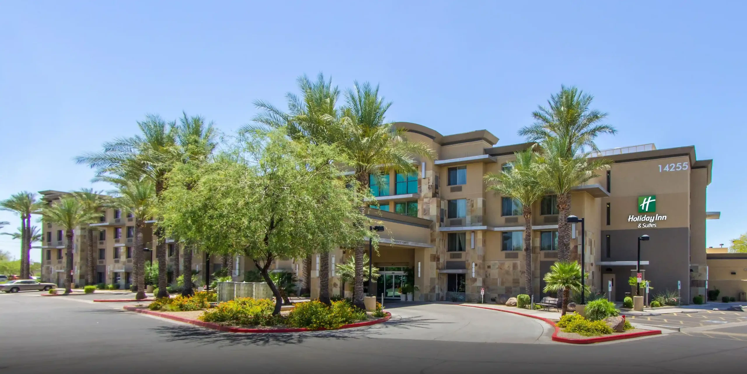 Front exterior of Holiday Inn & Suites Scottsdale North – Airpark with palm trees and driveway
