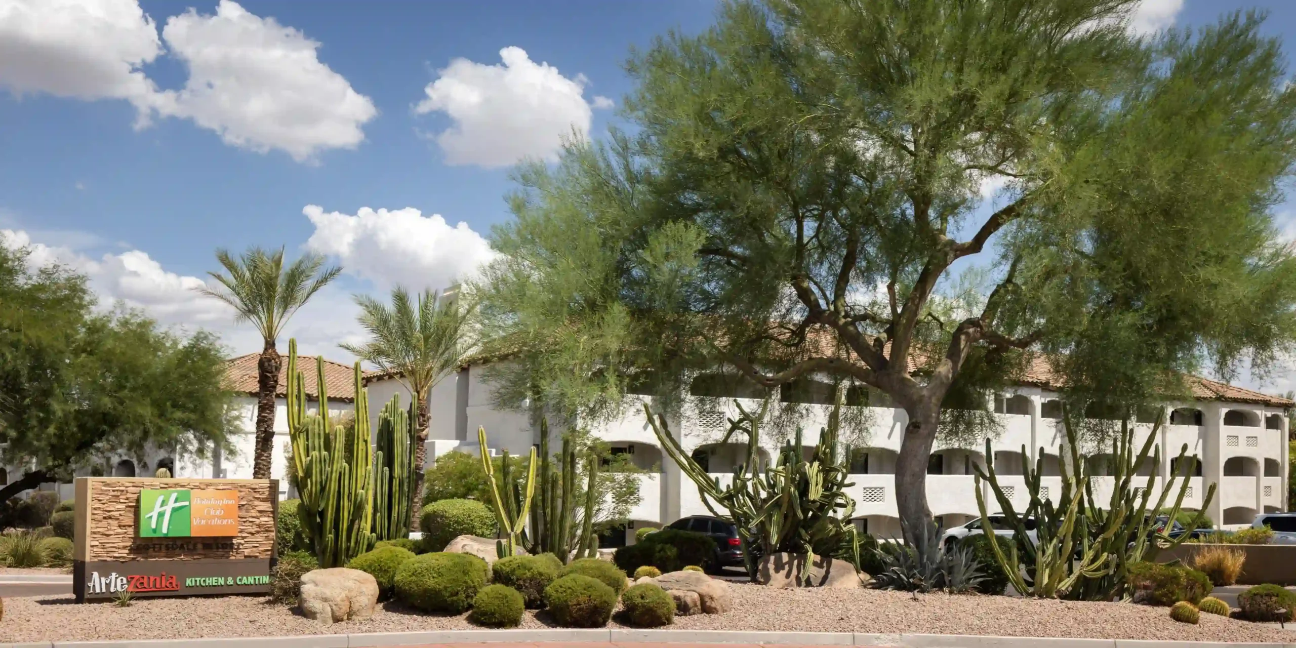 Exterior view of Holiday Inn Club Vacations Scottsdale Resort with desert landscaping and cacti under blue sky.