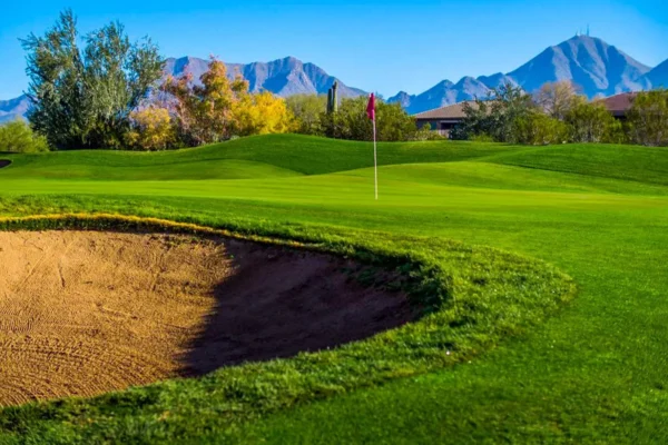 Sand bunker and green with flag overlooking McDowell Mountains under clear blue sky at McDowell Mountain Golf Club.