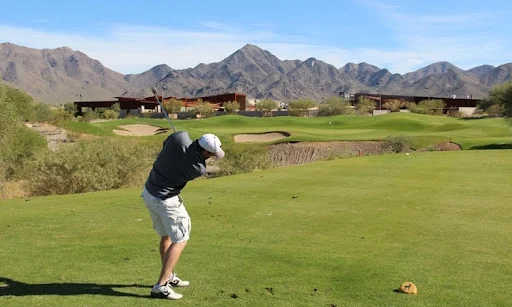 Golfer taking a swing on the fairway with McDowell Mountains rising in the background at McDowell Mountain Golf Club.