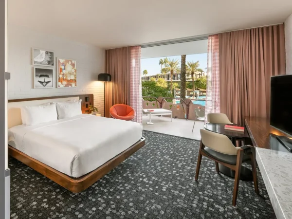 Modern guest room at Hotel Valley Ho in Scottsdale featuring a king bed, work desk, and an open balcony with palm and pool views.